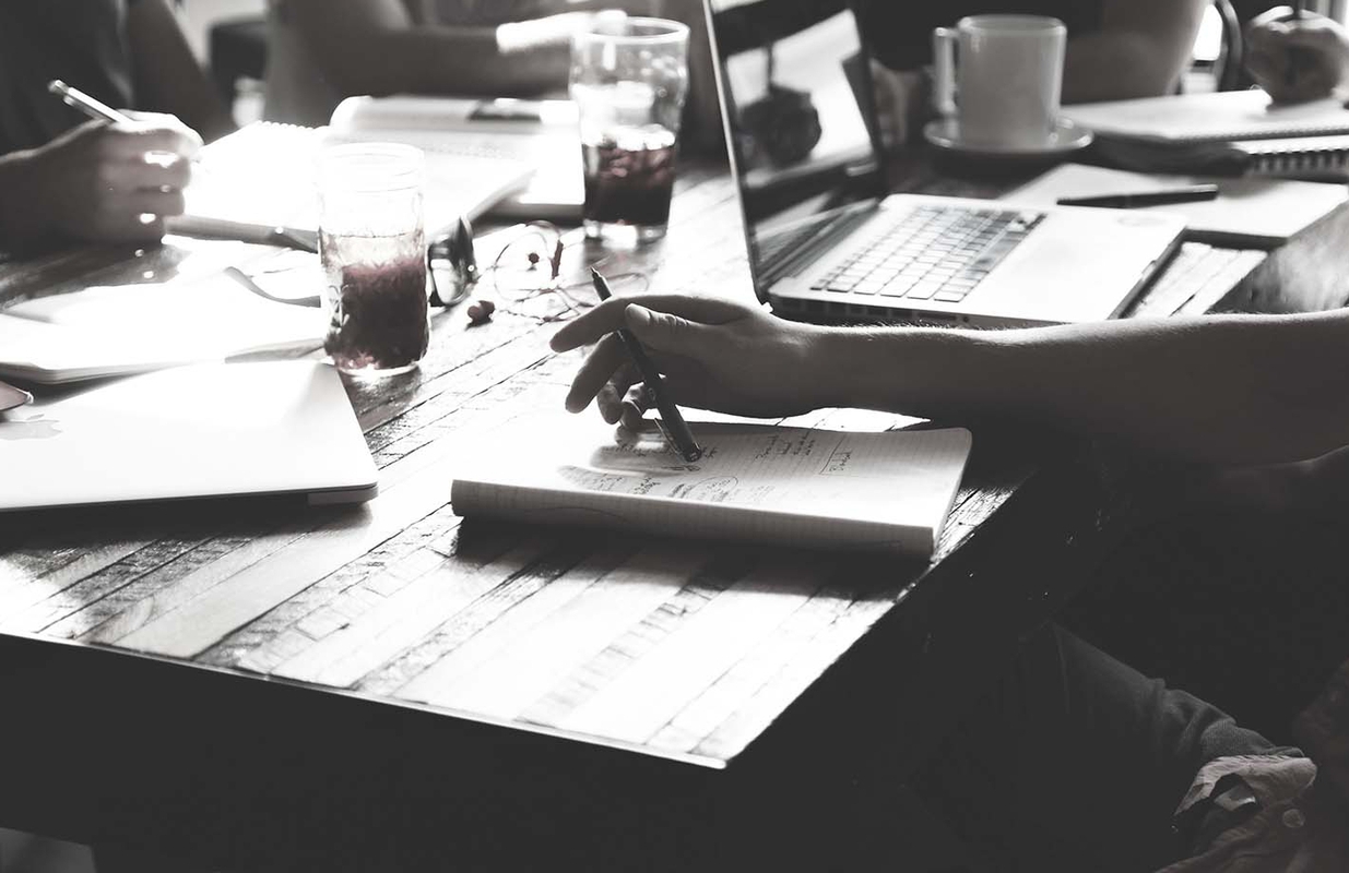 People sitting around a table with notebooks, pens, computers and coffee